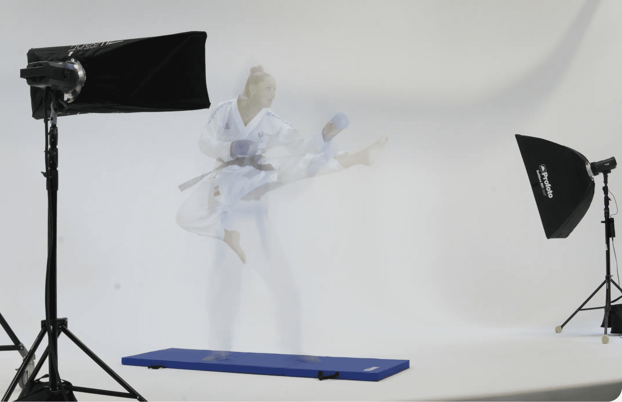 Karate athlete Alizée Agier performing a flying kick with a motion blur effect on a studio set with visible lighting equipment.