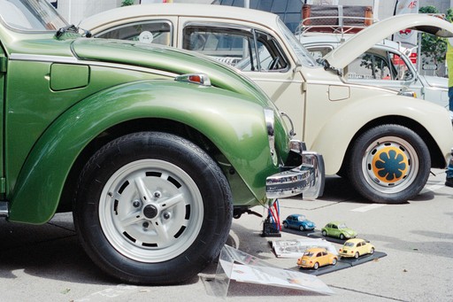 Two classic volkswagen beetles, one green, one cream.