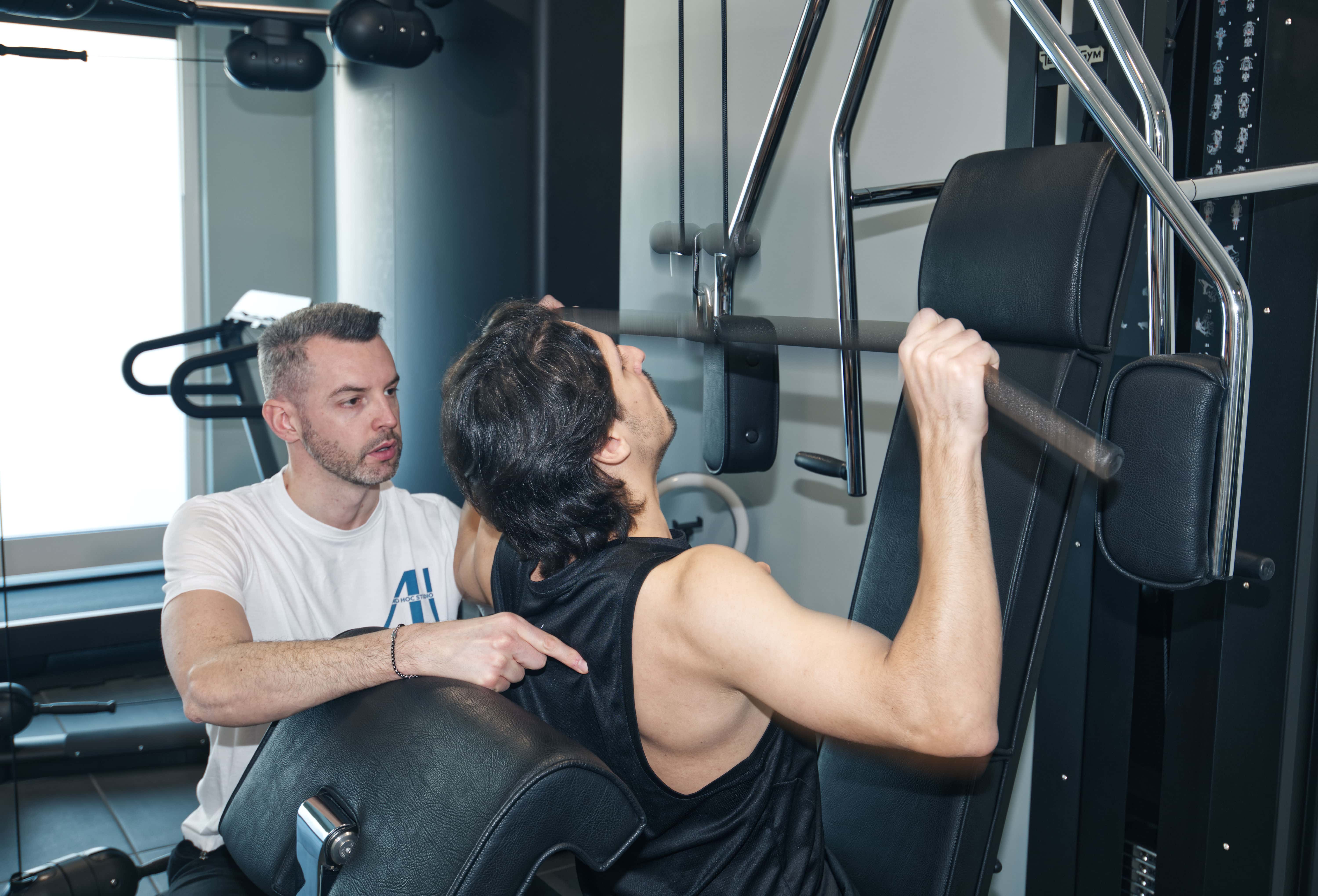 A person in a white outfit sits on a round stool in a spacious, minimalist room. The wall is covered with framed photos surrounding a large screen, creating a serene, contemplative atmosphere