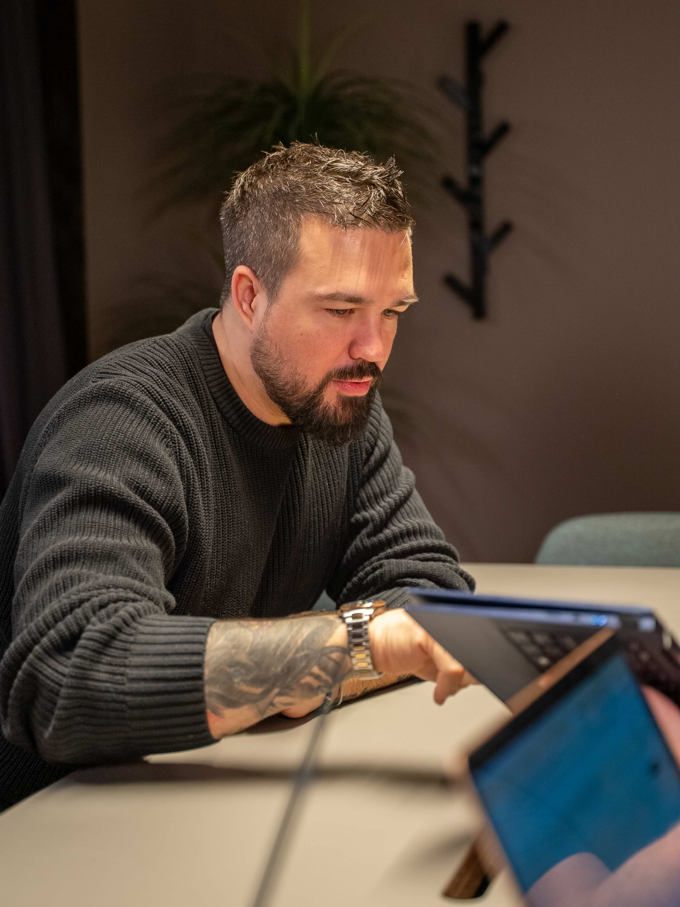 Man in a sweater smiling with arms crossed while standing by a wooden wall.