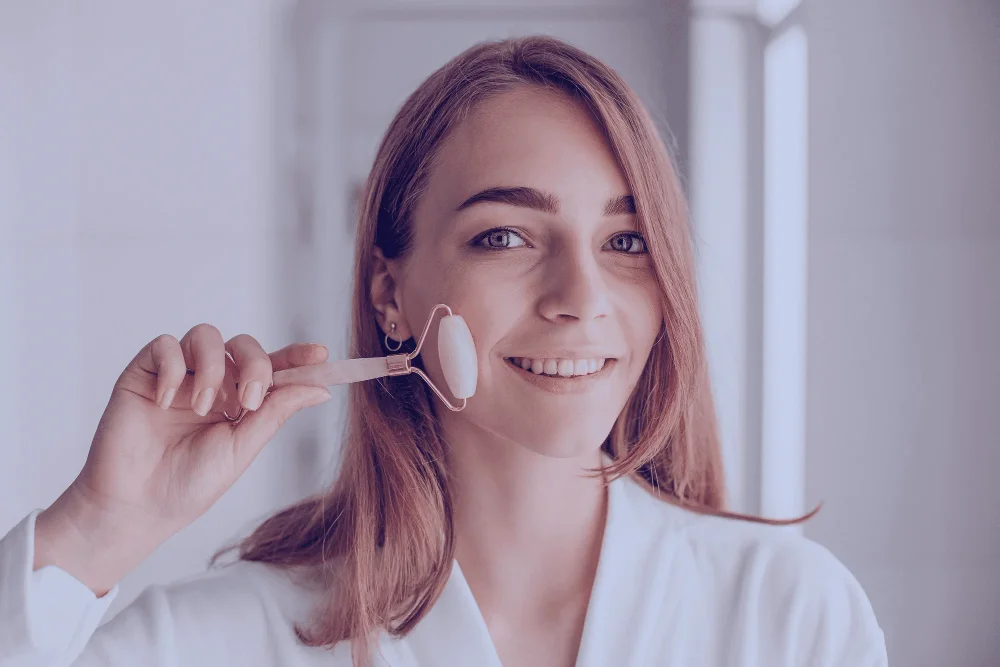 Smiling woman holding a rose quartz face roller, using it for a self-massage on her face