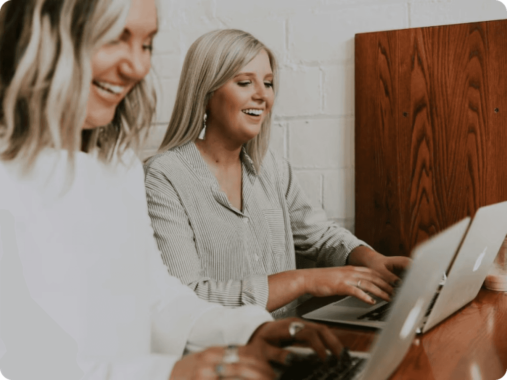 Two women working on laptops at a table, engrossed in their tasks.