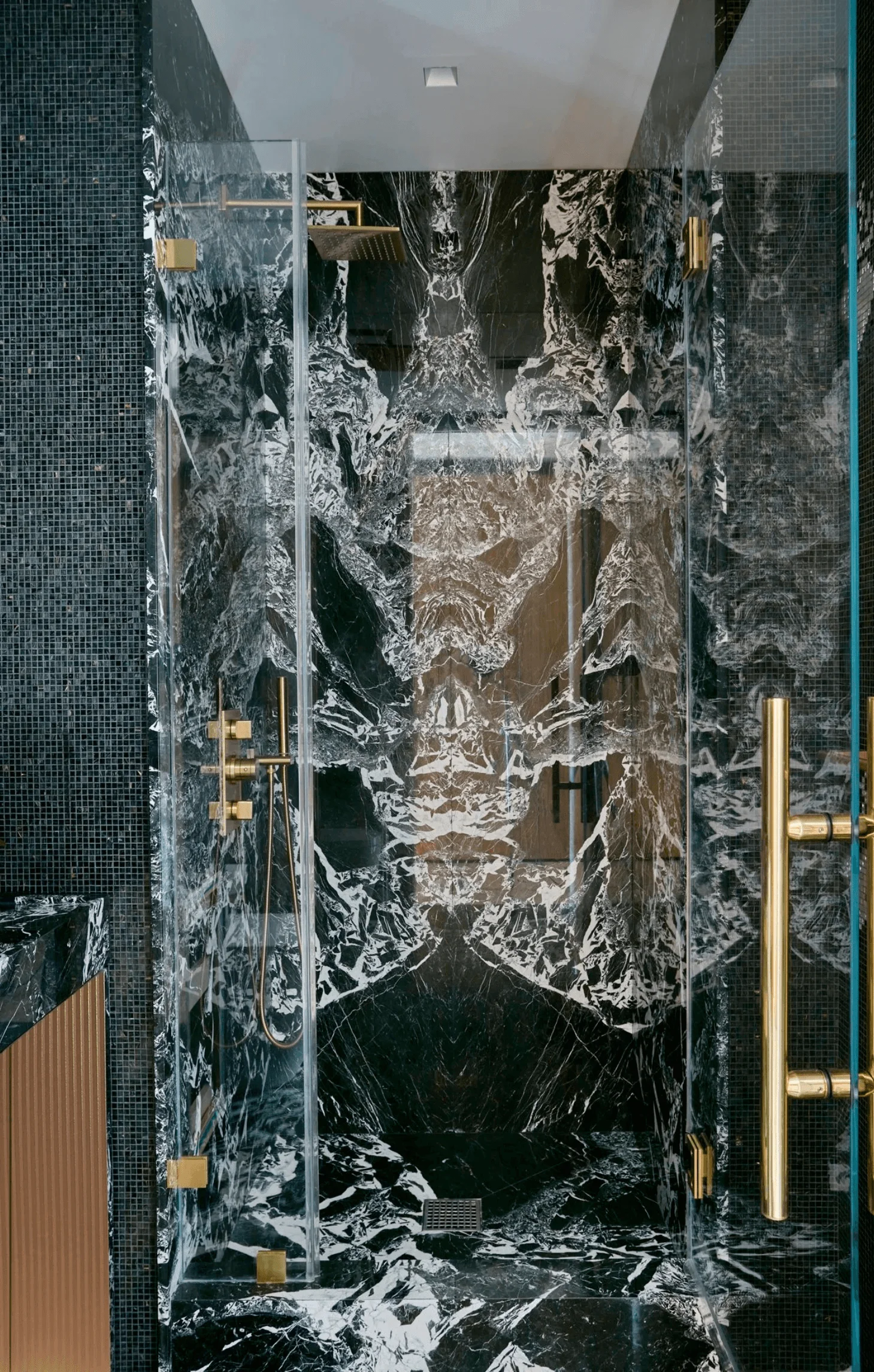 A glass-enclosed shower lined in dramatic black and white marble with brass fittings
