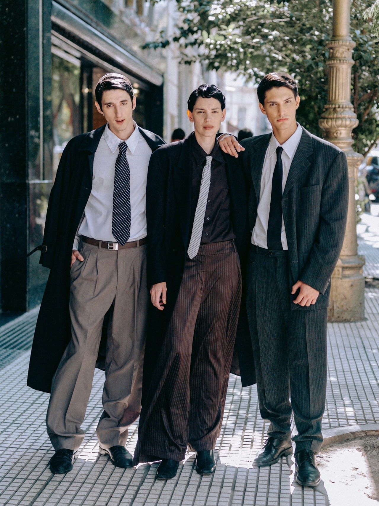 Three friends standing together on a street, getting photographed.