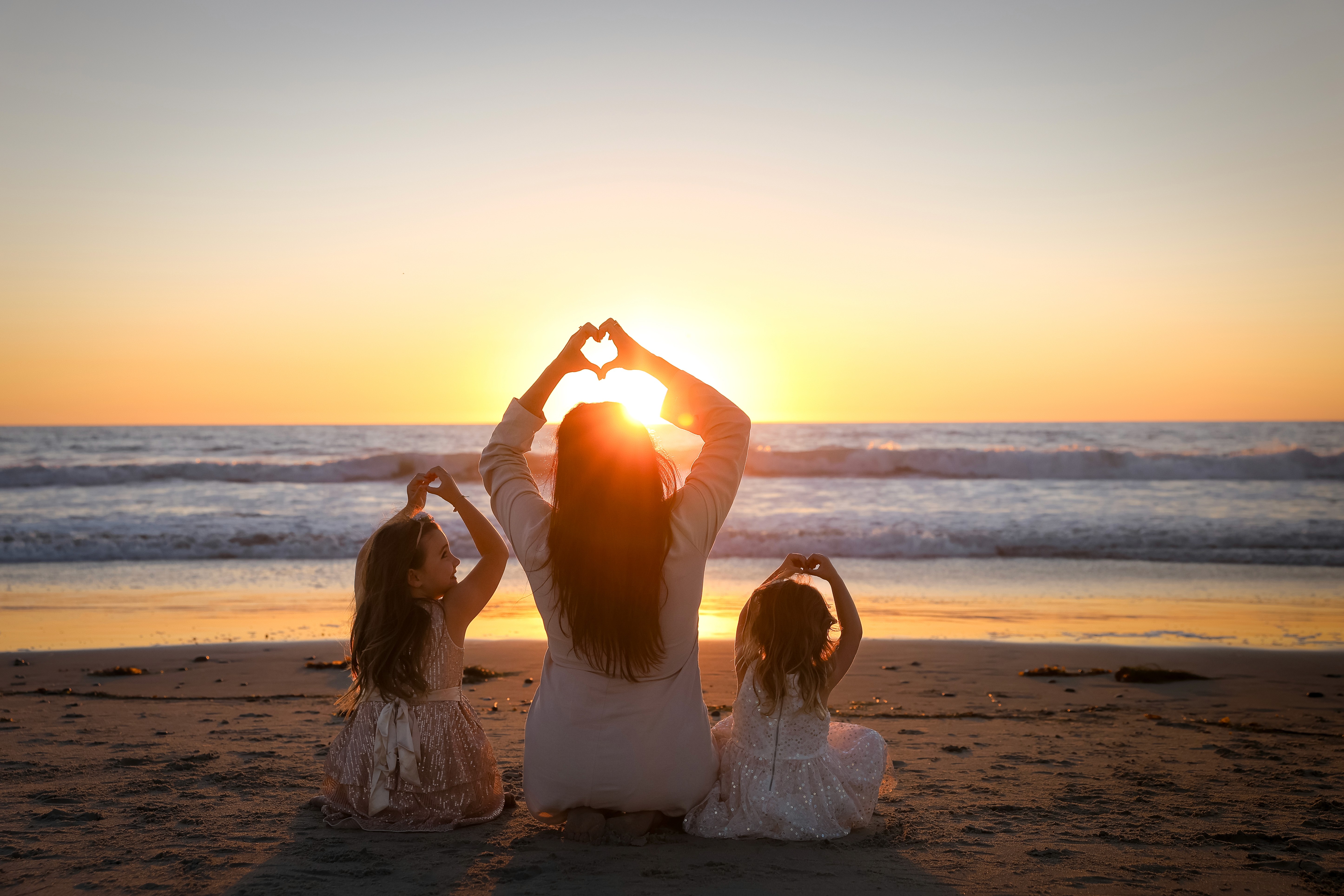 Mother and daughters making a heart shape at the beach at sunset