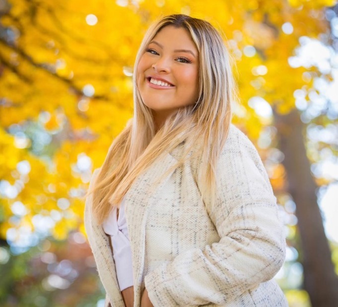 A student poses for a photo with yellow fall foliage