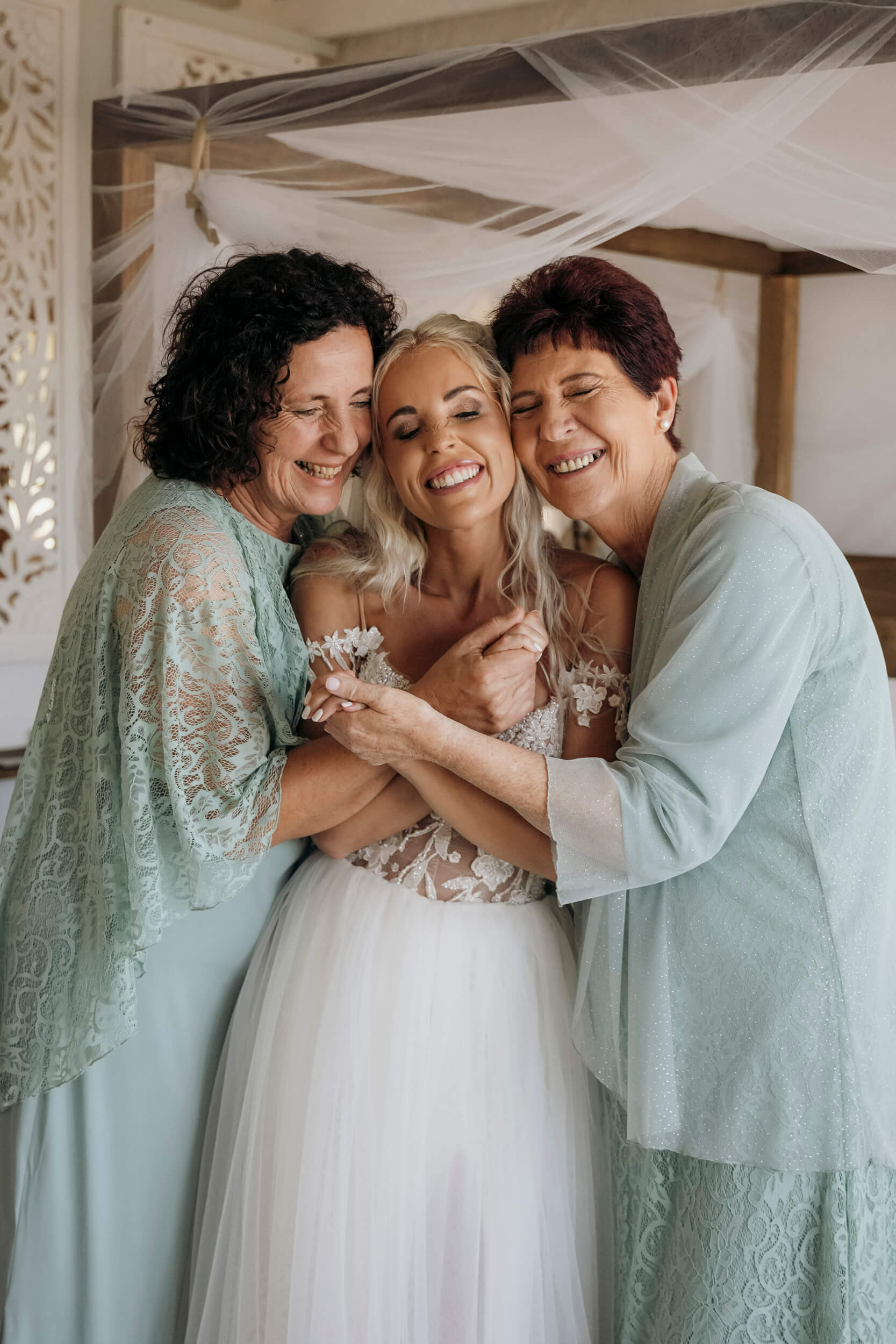 Bride’s mother and groom’s mother-in-law hugging bride before wedding ceremony