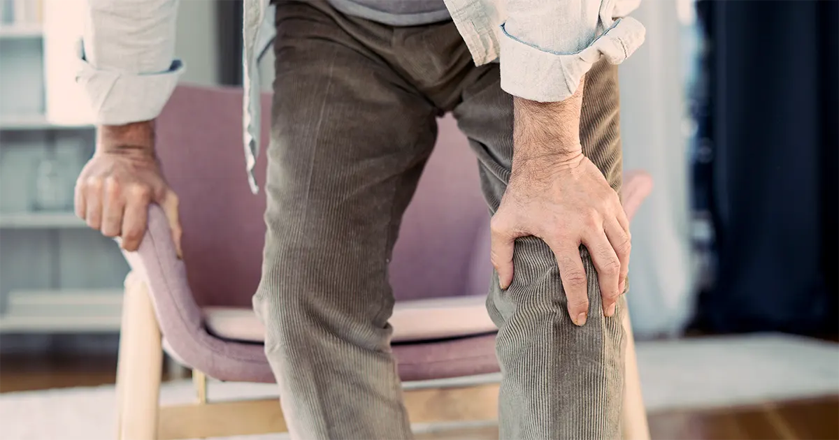 En mann som holder på sitt venstre kne på grunn av av smerte.