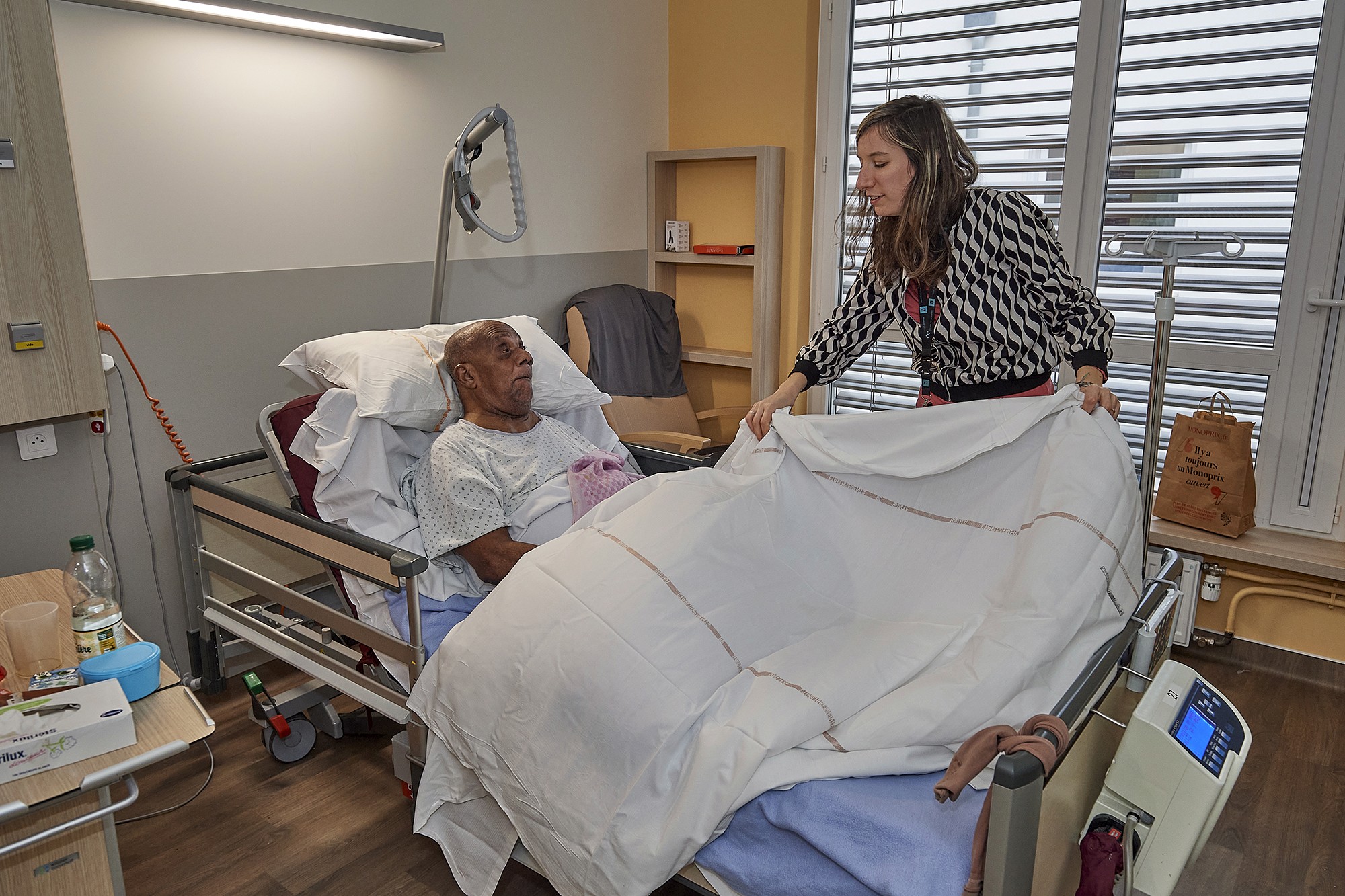 Mise en place d’un drap de protection avant que Saïko monte sur le lit.. Un moment très attendu pour les patients alités.