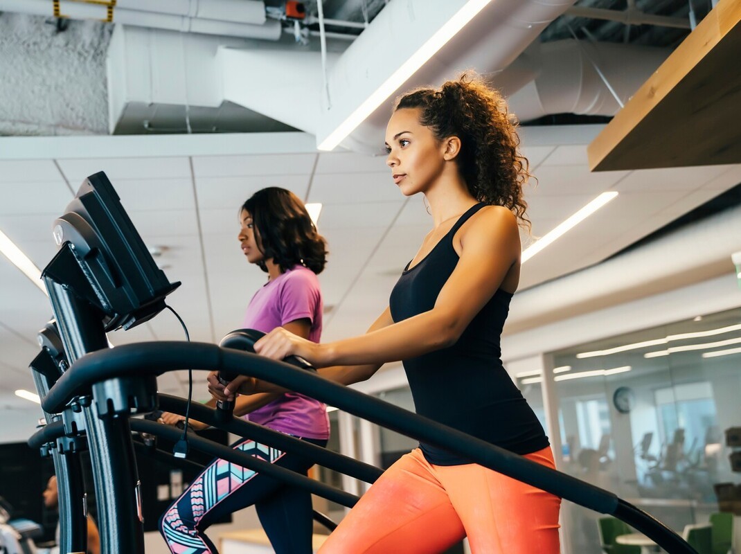 “pair of women in athletic gear using a StairMaster for weight loss as part of their gym routine