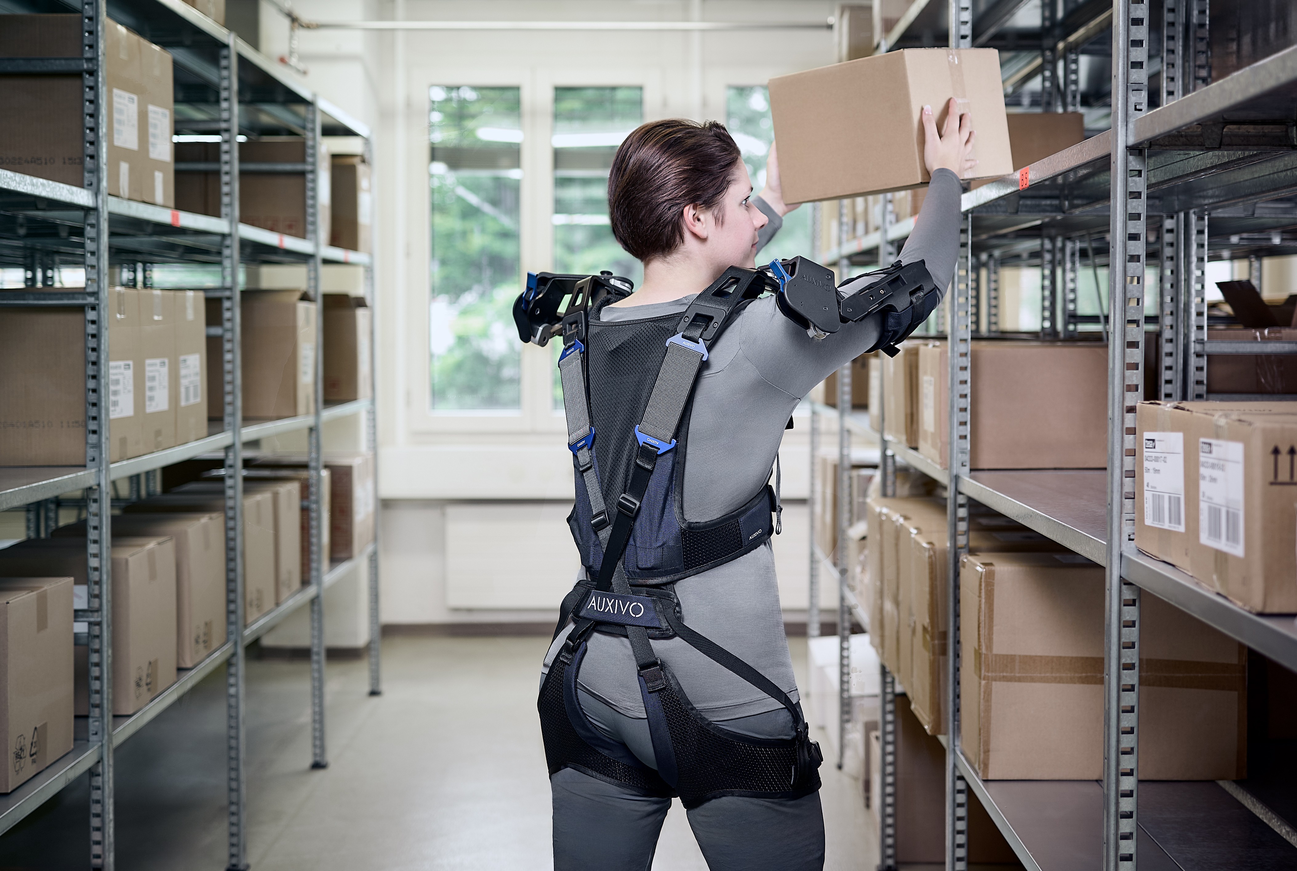 Two warehouse workers using the OmniSuit exoskeleton to lift and move wooden pallets with less effort.