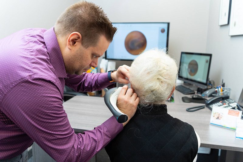 A healthcare professional examines the ear of an elderly patient in a clinical setting.