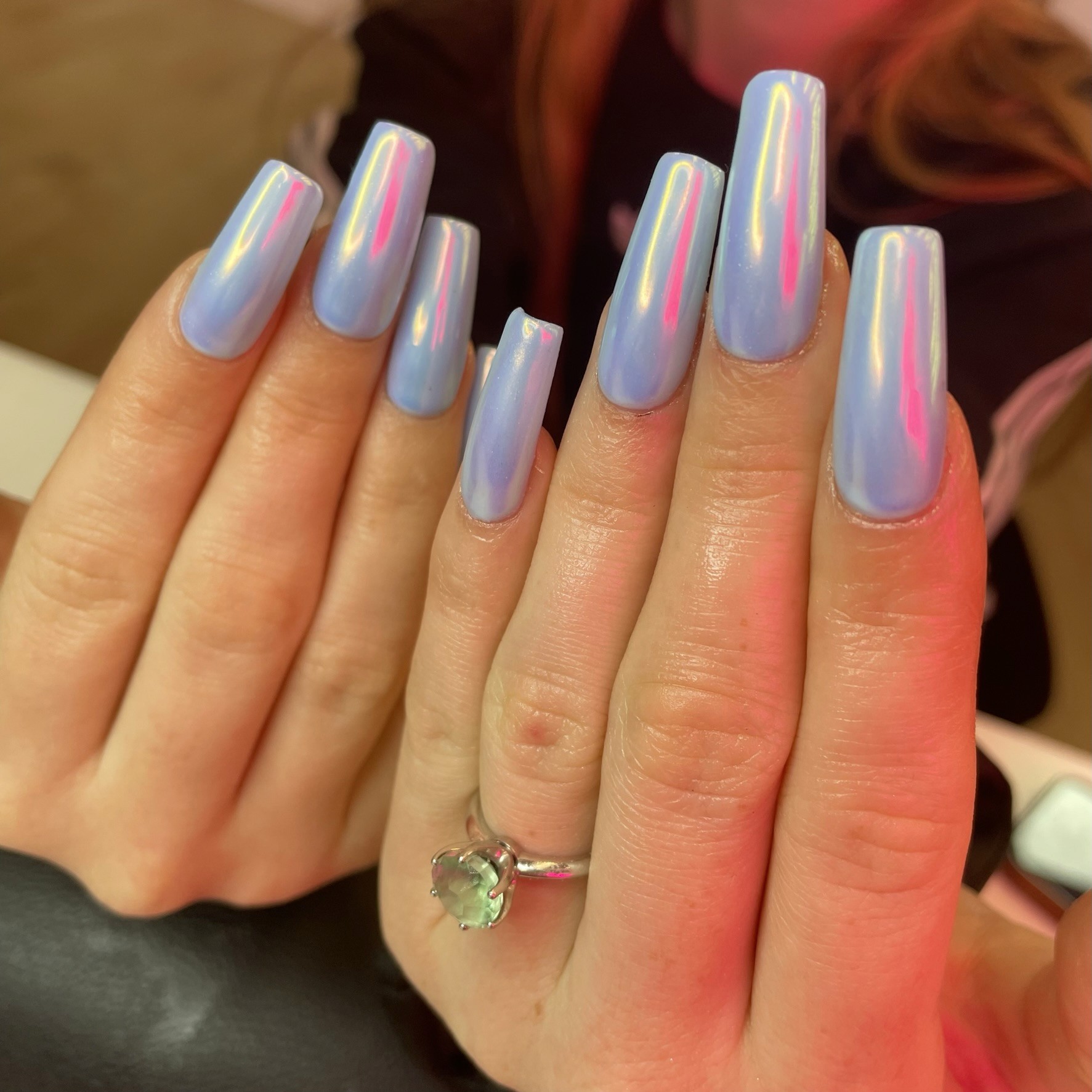 Long coffin-shaped nails in a soft periwinkle blue with a high-shine holographic chrome finish that shifts to pink and gold in the light.