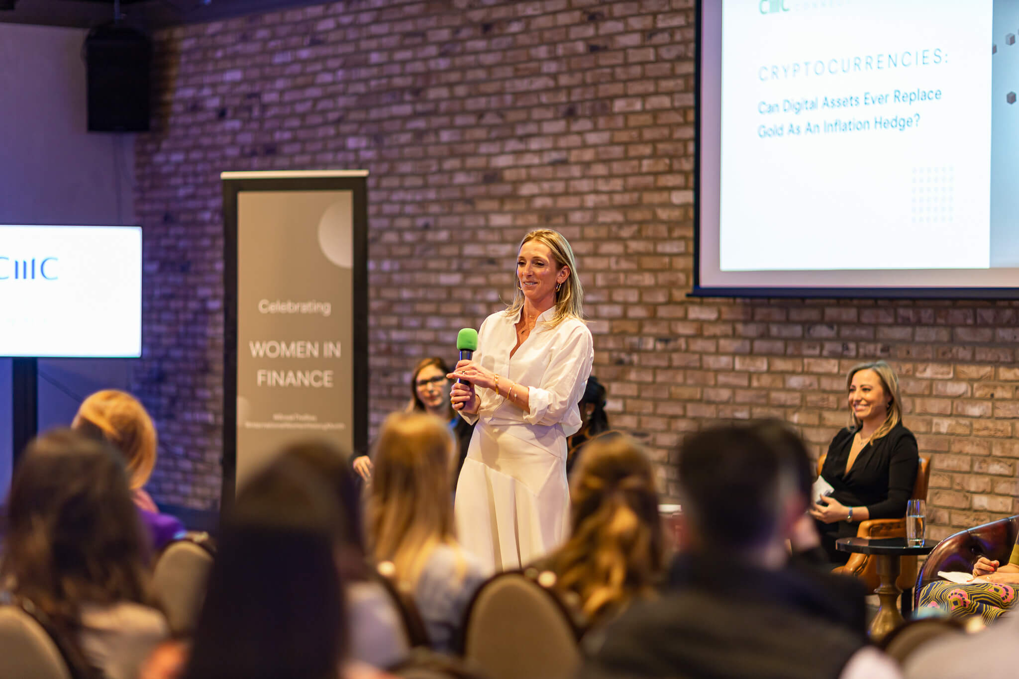 Professional women in finance networking event with keynote speaker presenting to an audience during a business conference panel discussion