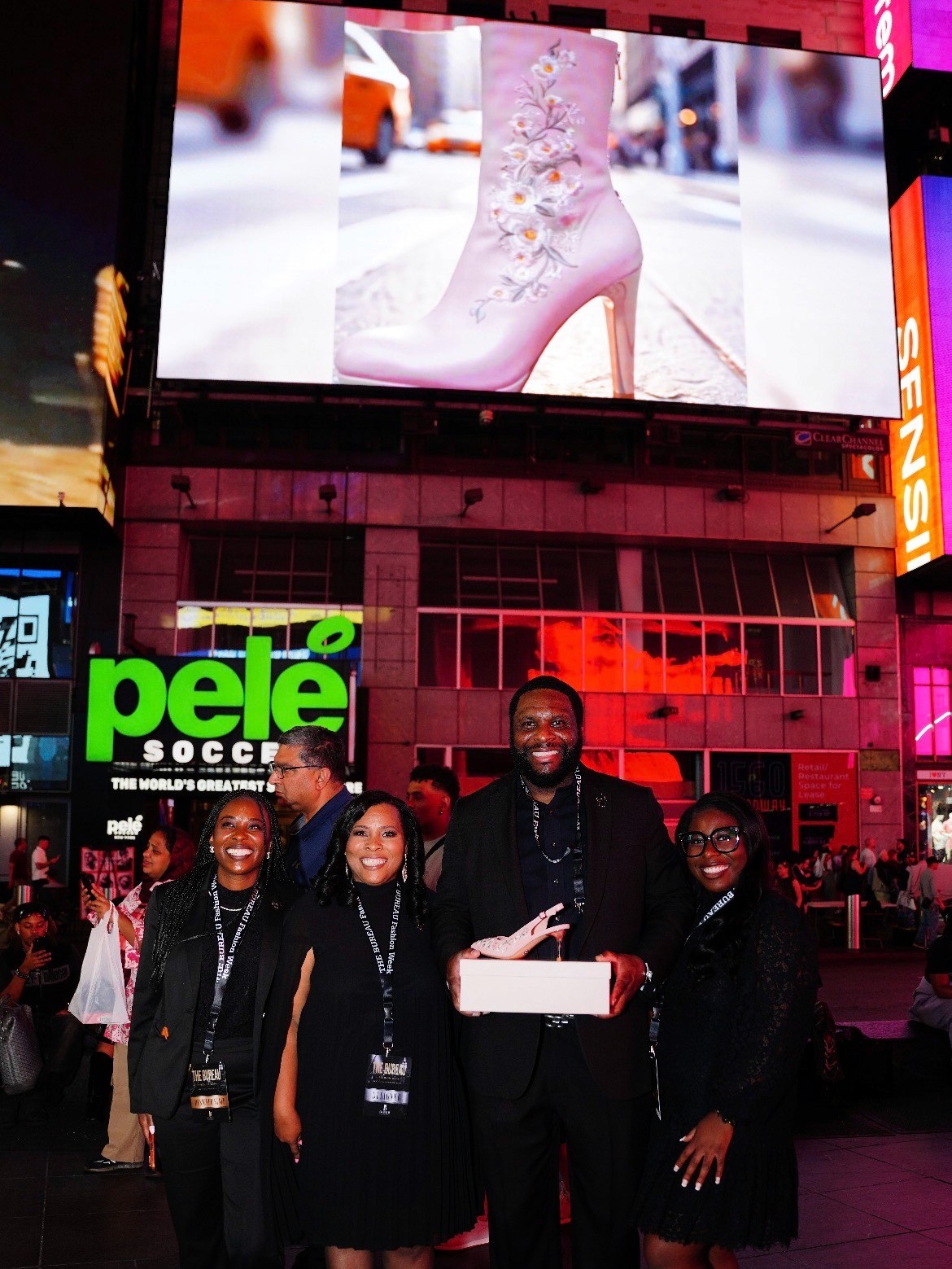 Strawberry Flowers team posing beneath a Times Square billboard displaying a pink floral boot.