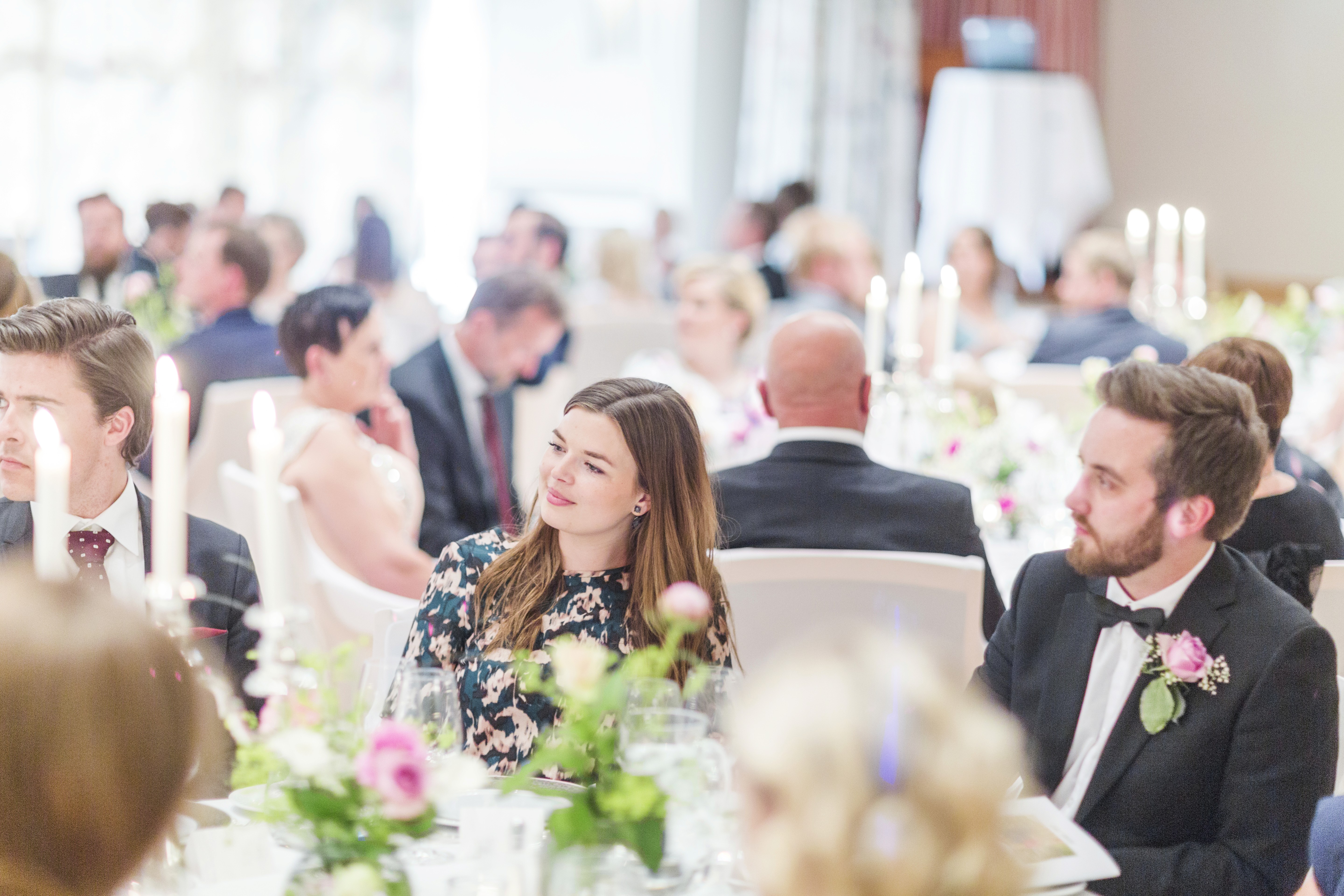 Spacious conference room with rows of wooden tables and blue cushioned chairs, large windows allowing natural light to illuminate the space, and ceiling lights for additional brightness, creating an ideal setting for professional meetings or seminars.