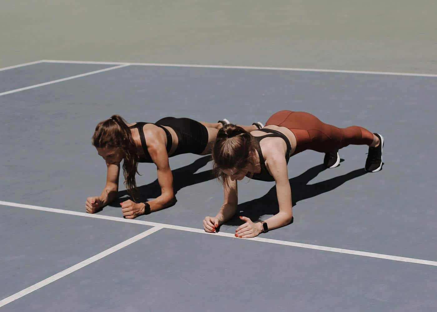 Two women doing planks on their forearms on a tennis court