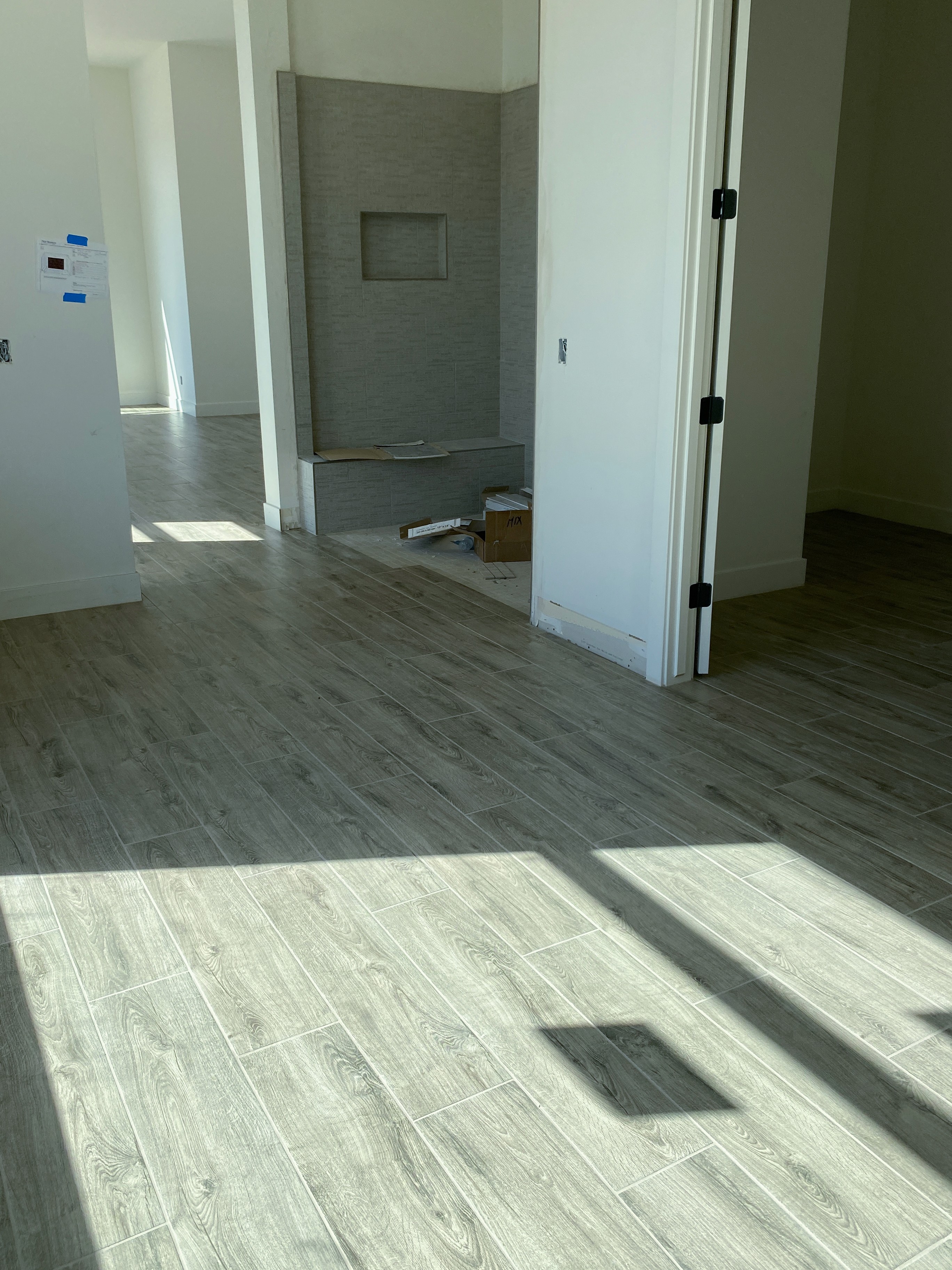 Modern bathroom with wood-look tile flooring, white walls, and natural light in a new home under construction.