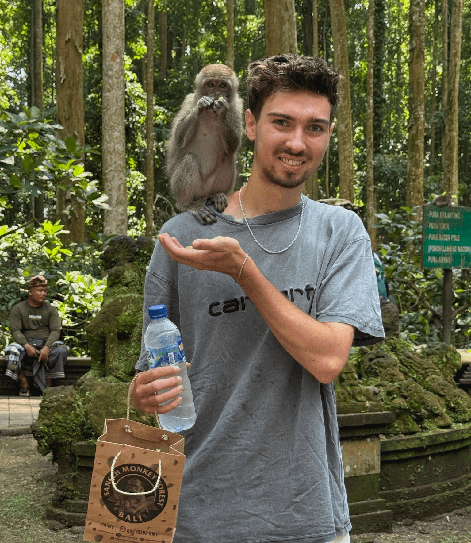 A young person with curly hair smiles at the camera while sitting in front of a laptop against a dark background.