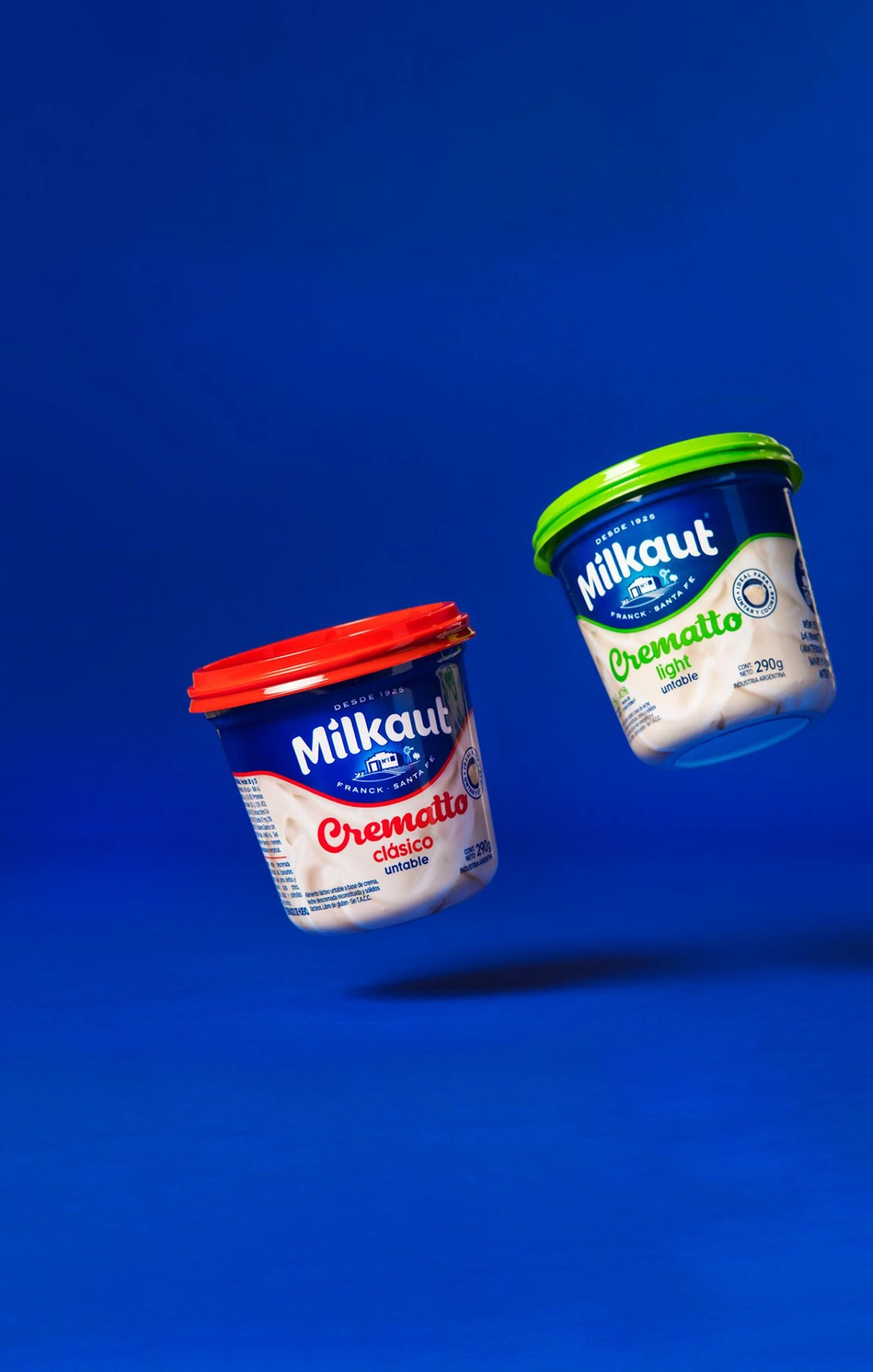 Two tubs of yogurt are hovering against a blue background, showcasing colorful packaging.