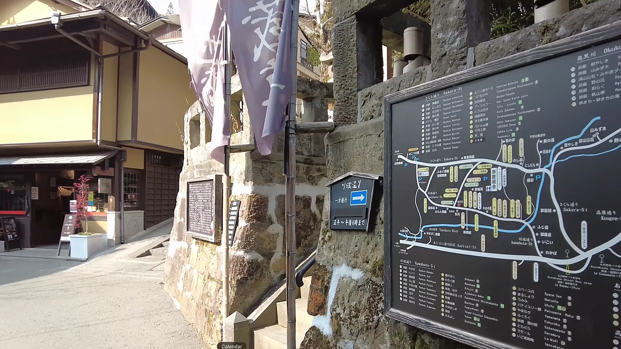 A village street at Kurokawa Onsen with a map noticeboard and banner flags