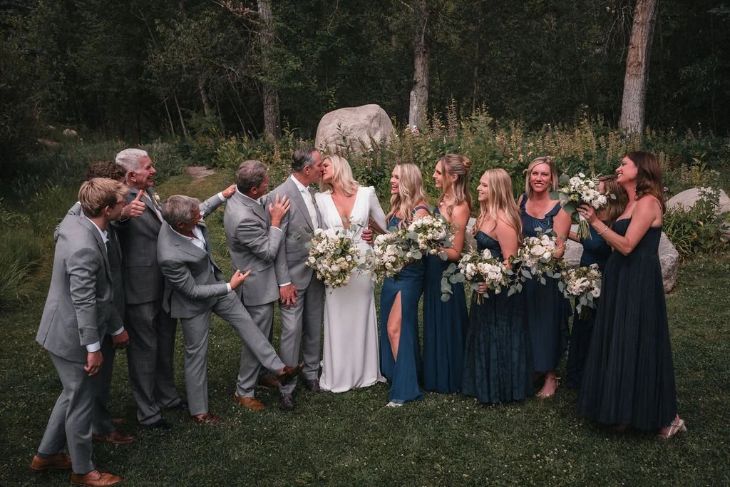 Wedding party gathered around the newlyweds in a wooded garden