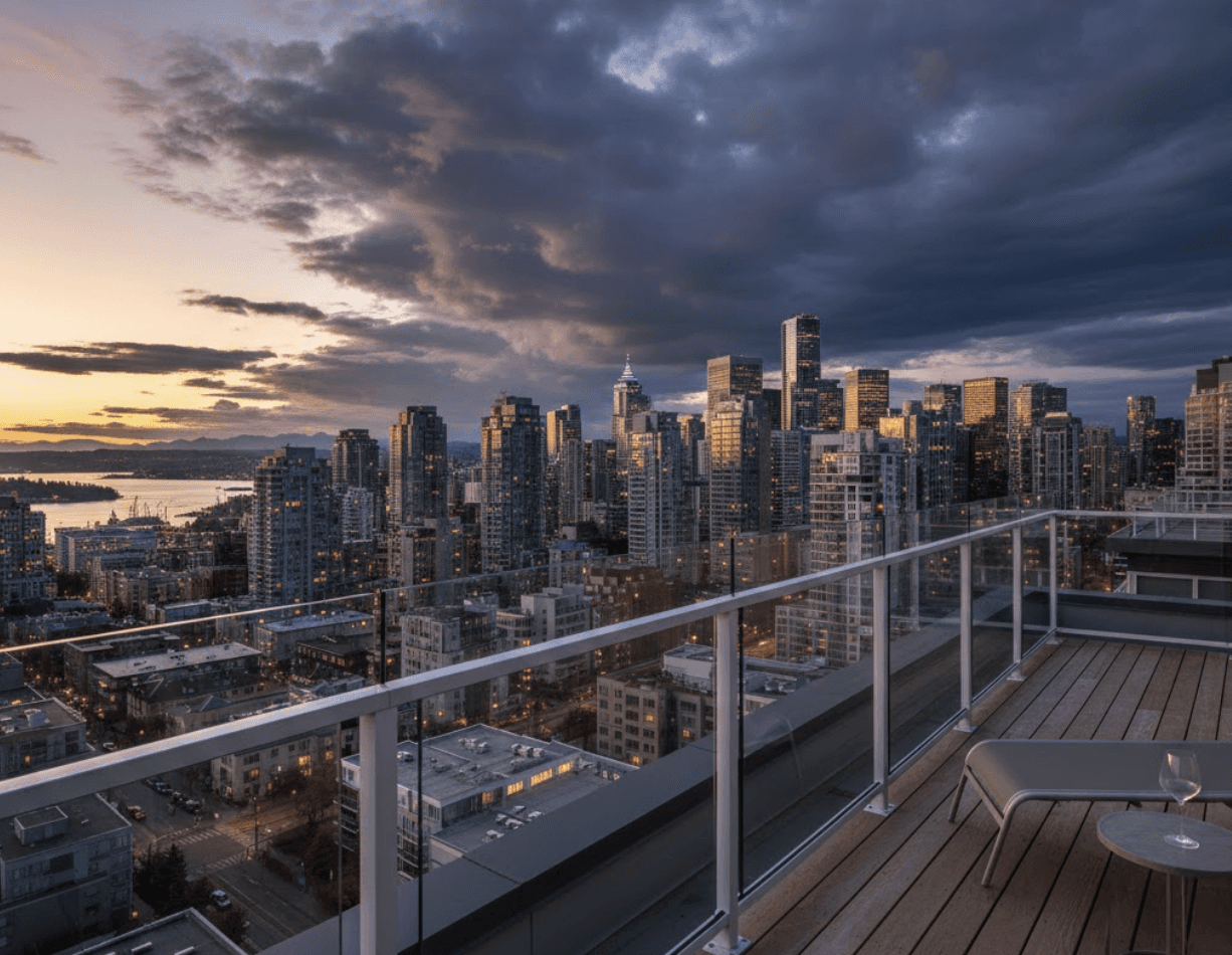 First-person perspective standing on townhouse rooftop deck with frameless glass railings wrapping the perimeter, downtown Vancouver skyline in background, dramatic clouds, wide angle lens, glass so clear it nearly disappears, emphasis on unobstructed 180-degree views, lifestyle real estate photography