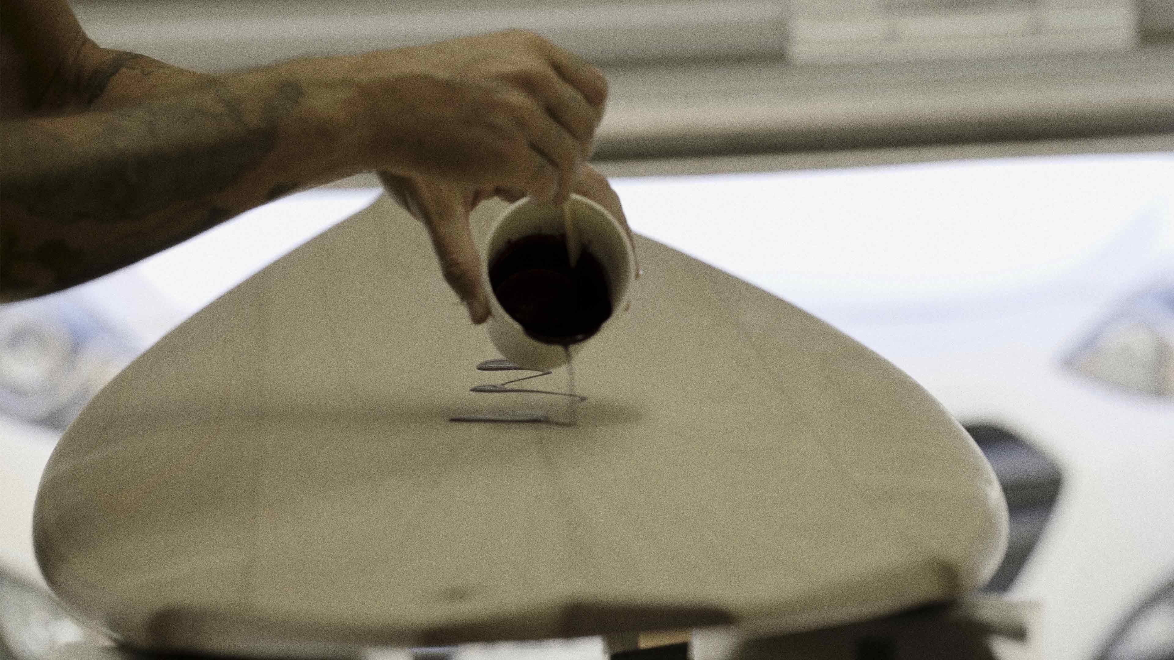 Man pouring stain on a wooden surfboard