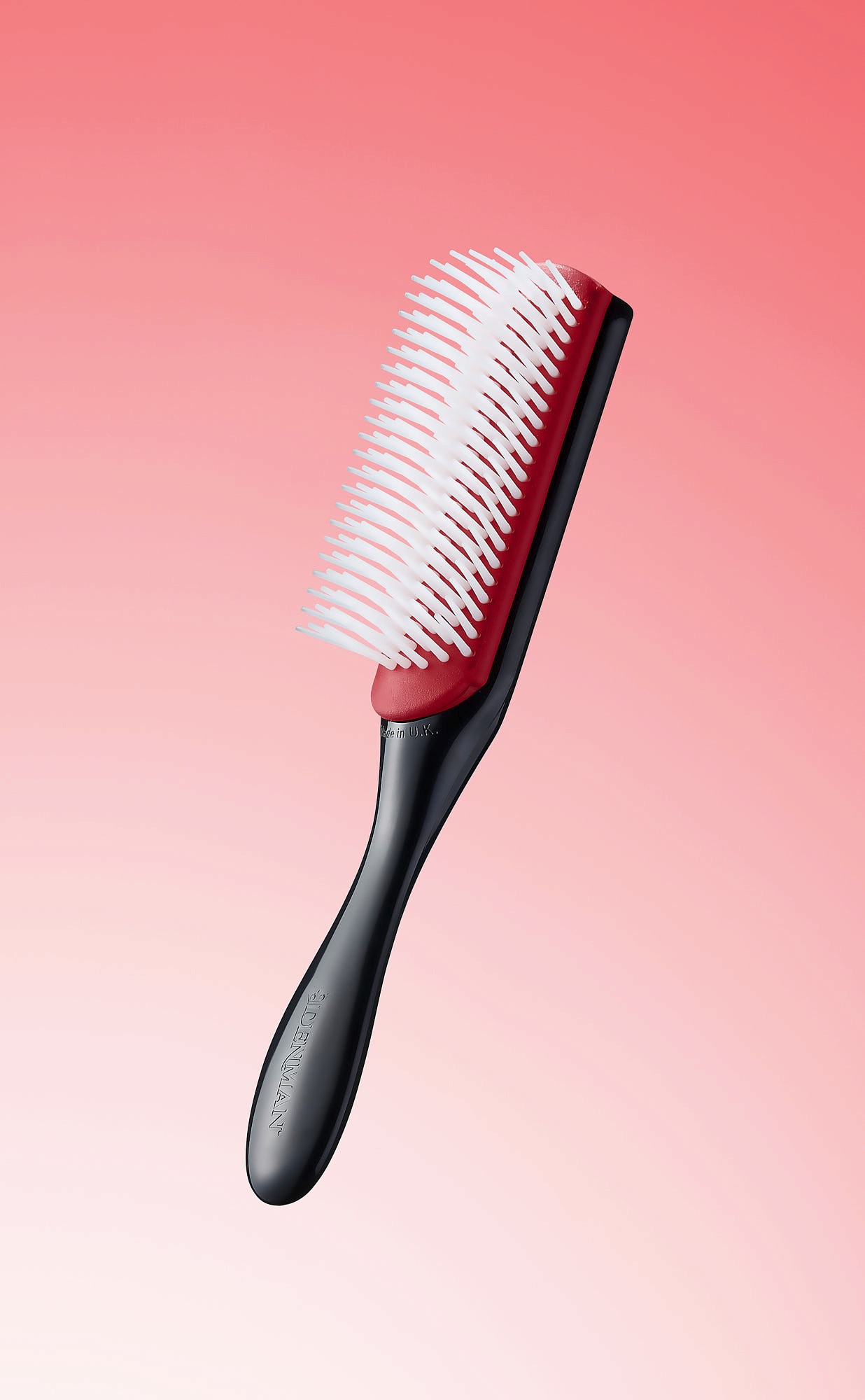 A hairbrush with a pink bristle section and a black handle, set against a soft pink gradient background.