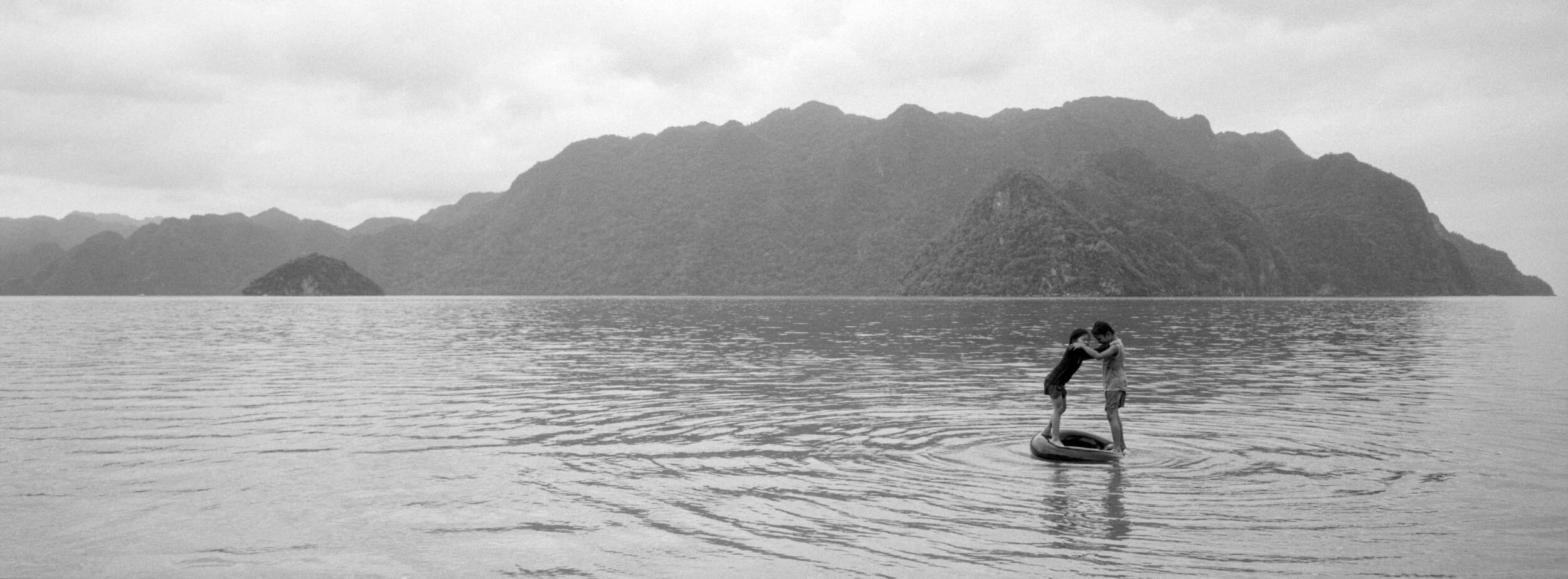 Black and white panoramic film photograph captured on a Hasselblad XPan, depicting two children playing with an inflated tire in the Philippines, showcasing the camera's unique wide-format cinematic aesthetic for landscape and documentary photography