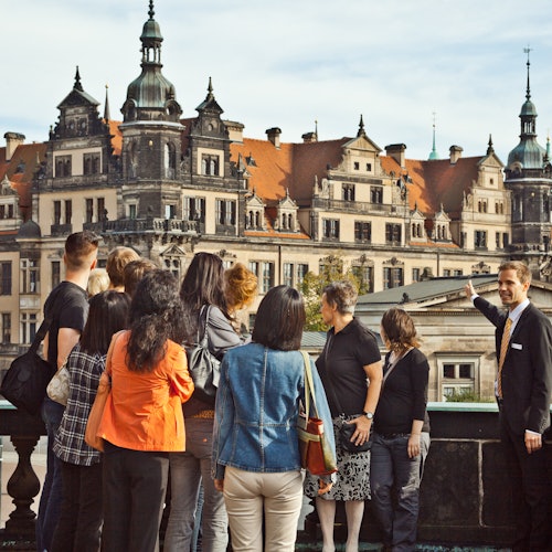 Opas viittoo koristeelliseen, historiallisesti merkittävään rakennukseen puhuessaan turistiryhmälle.