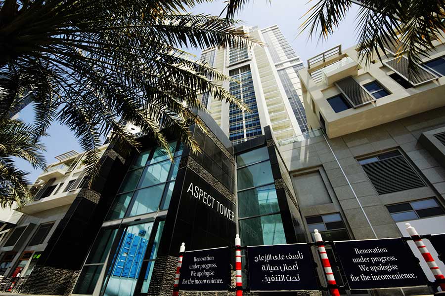 Close-up details of a building entrance with signage, as seen through tropical palm tree fronds.