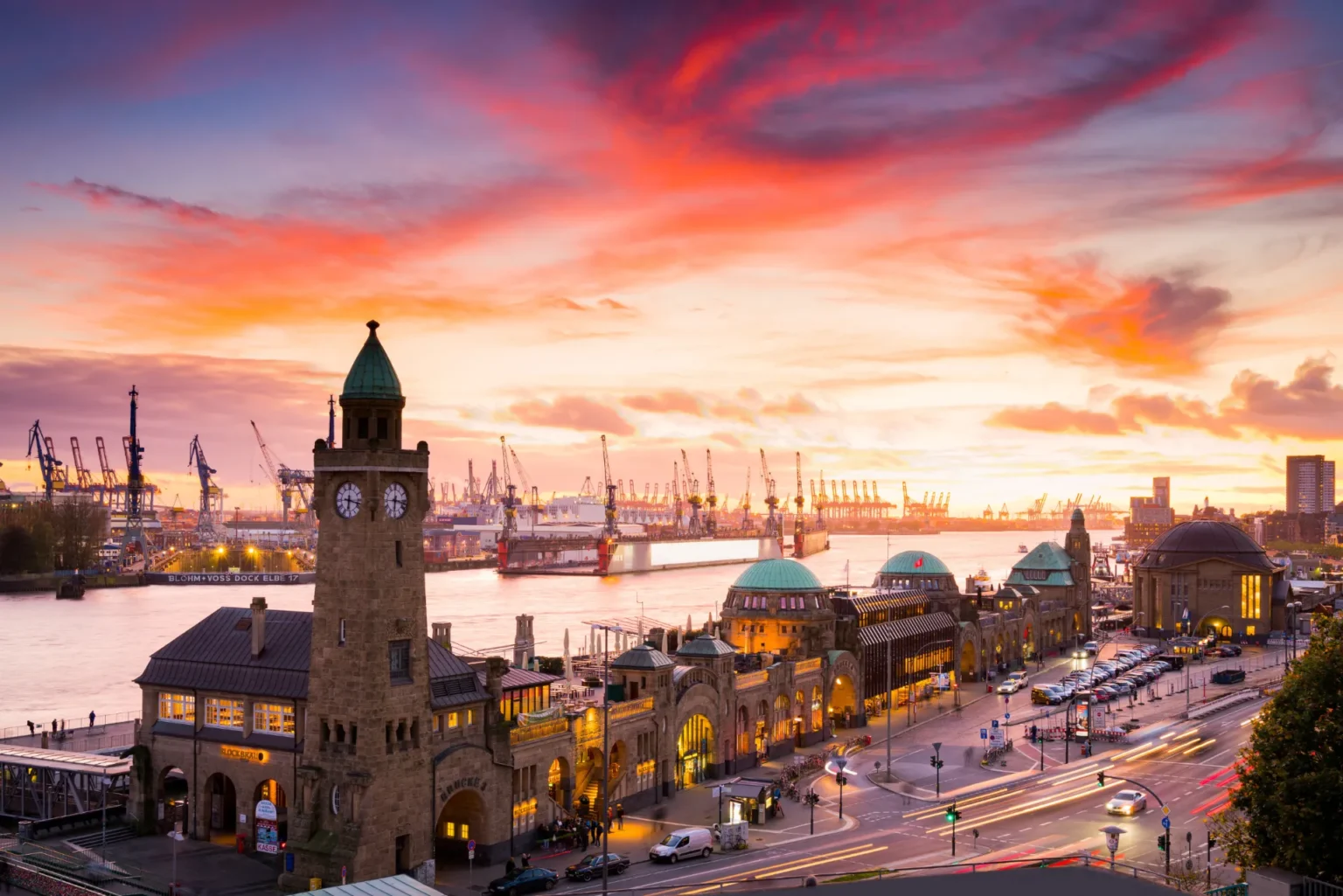 Sunset over a cityscape featuring a clock tower, with vibrant clouds and a snow-covered ground.