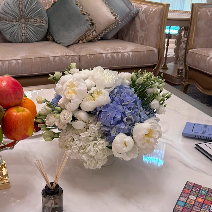 Elegant living room with marble coffee table, floral centerpiece, fruit stand, and designer books