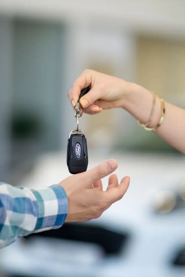 Person handing car keys to another, symbolizing the start of a car rental or car lease agreement.