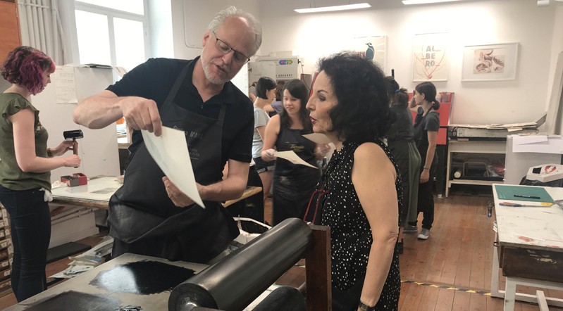 A photo of two people checking the ink and the paper while standing in a printing workshop.