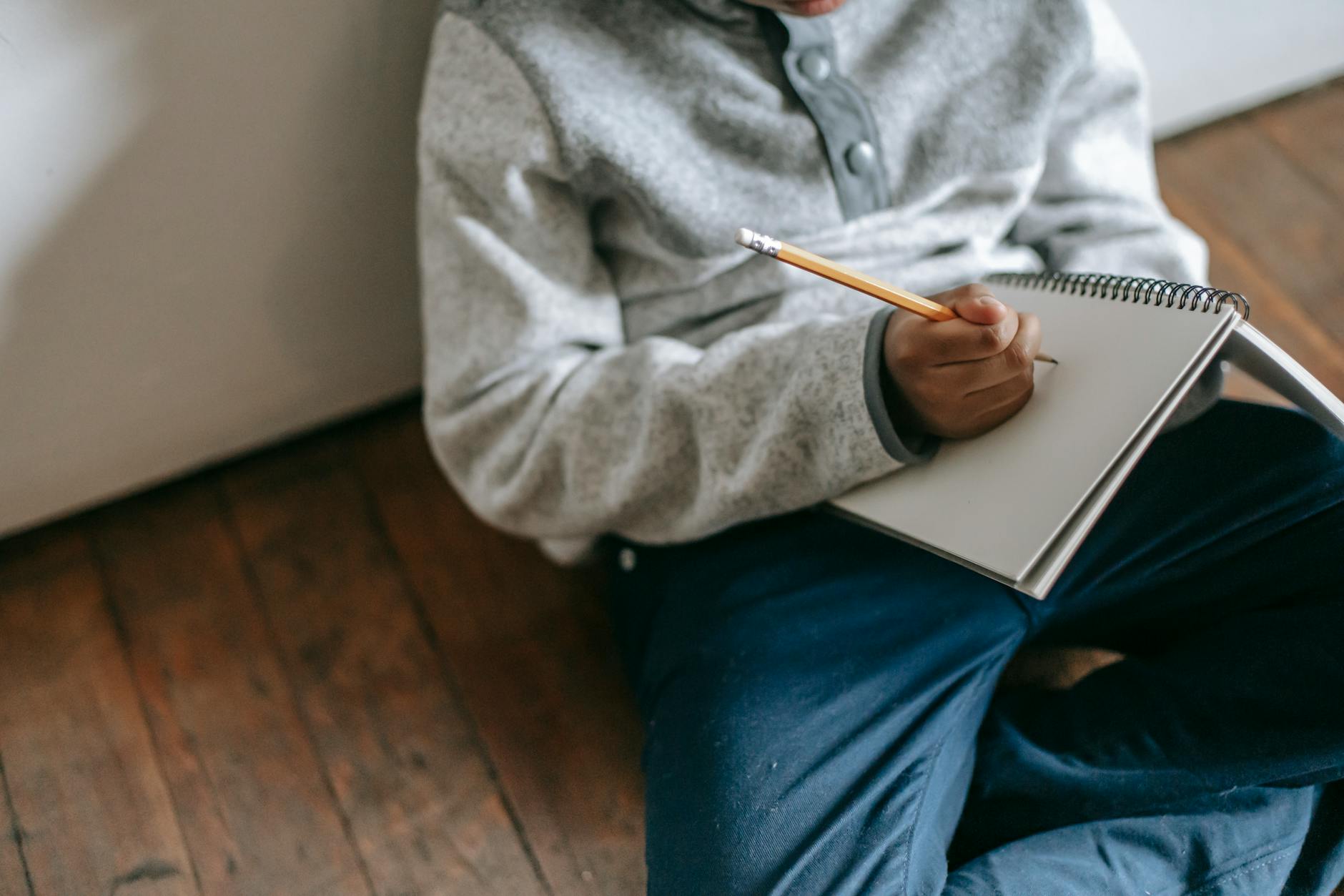 Close-up of a student's hand writing a self-reflection in a spiral notebook with a yellow highlighter nearby.