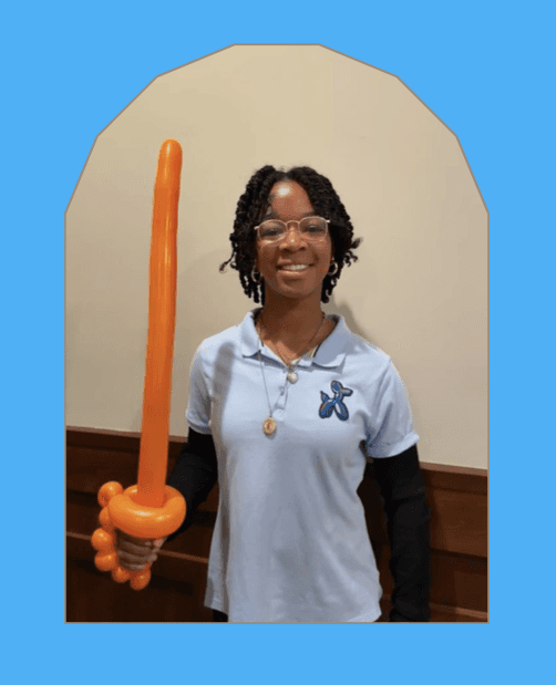 Elias smiling and posing with a black stickman balloon twist and a bucket of balloon twisting supplier