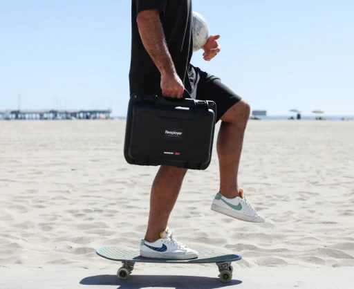 Person skateboarding on the beach while carrying a Reeplayer camera case, showing the portability and convenience of the equipment