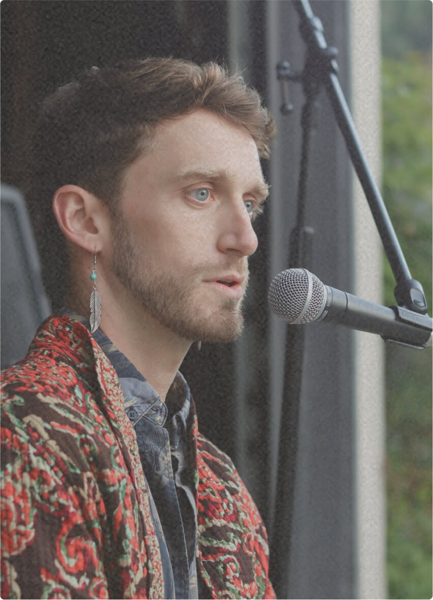 AwareHaus founder Emmett Patton speaking or signing into a mic, wearing a patterned shawl and feather earring.