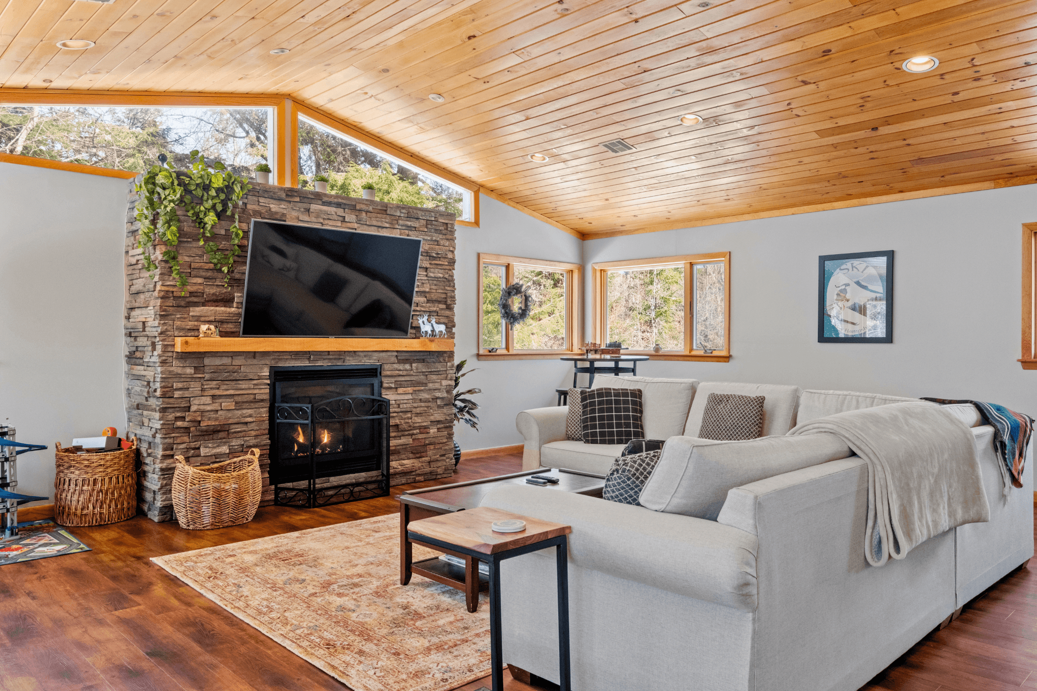 Cozy mountain chalet living room in Bartlett, NH with a gas fireplace set in a stone wall, vaulted wood ceiling, and a plush sectional sofa—perfect for family-friendly Airbnb stays near the White Mountains.