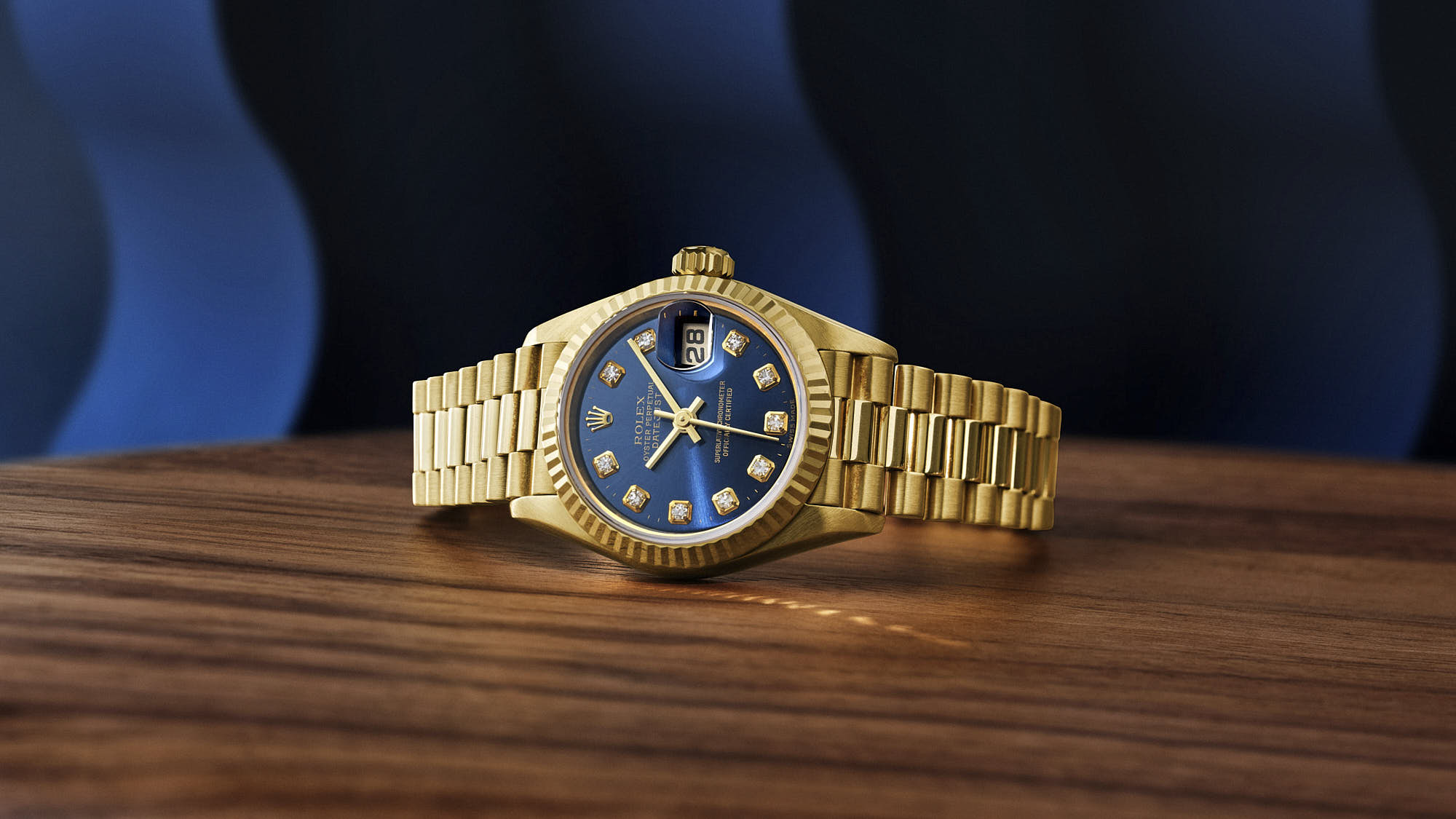 Luxury gold watch with blue dial and diamond markers on wooden surface.