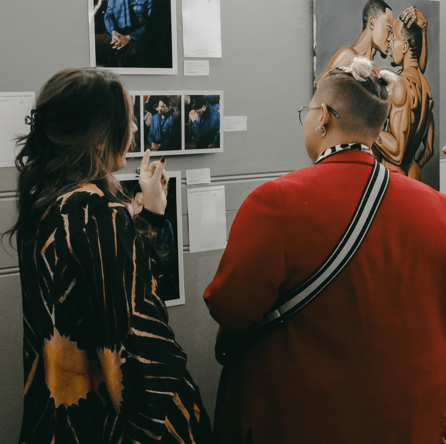 two people facing to the right, standing in front of two arworks