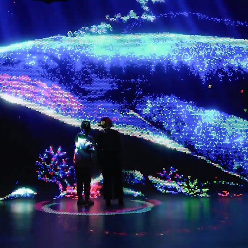 Two people stand in front of a large digital display showing a colorful, pixelated underwater scene with marine life.