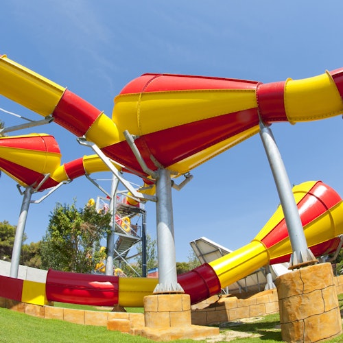 En färgglad, slingrande röd och gul vattenrutschbana på ett utomhusnöjesfält under en klarblå himmel.
