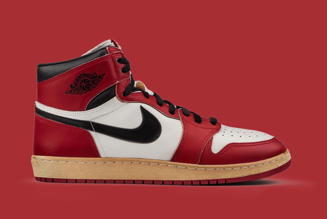 A close-up of a classic red and white Air Jordan 1 sneaker with a black Nike swoosh and a gum sole, set against a red background.