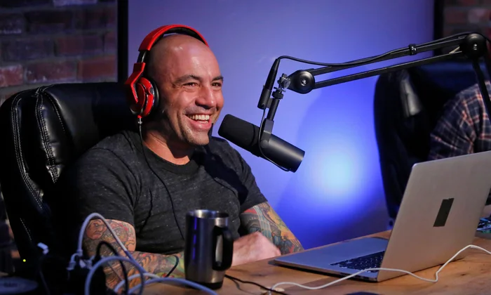 Man with red headphones laughing at a podcast desk with a microphone and laptop