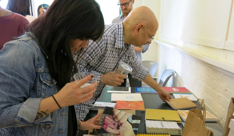 people picking up books and booklets from a table near a wall
