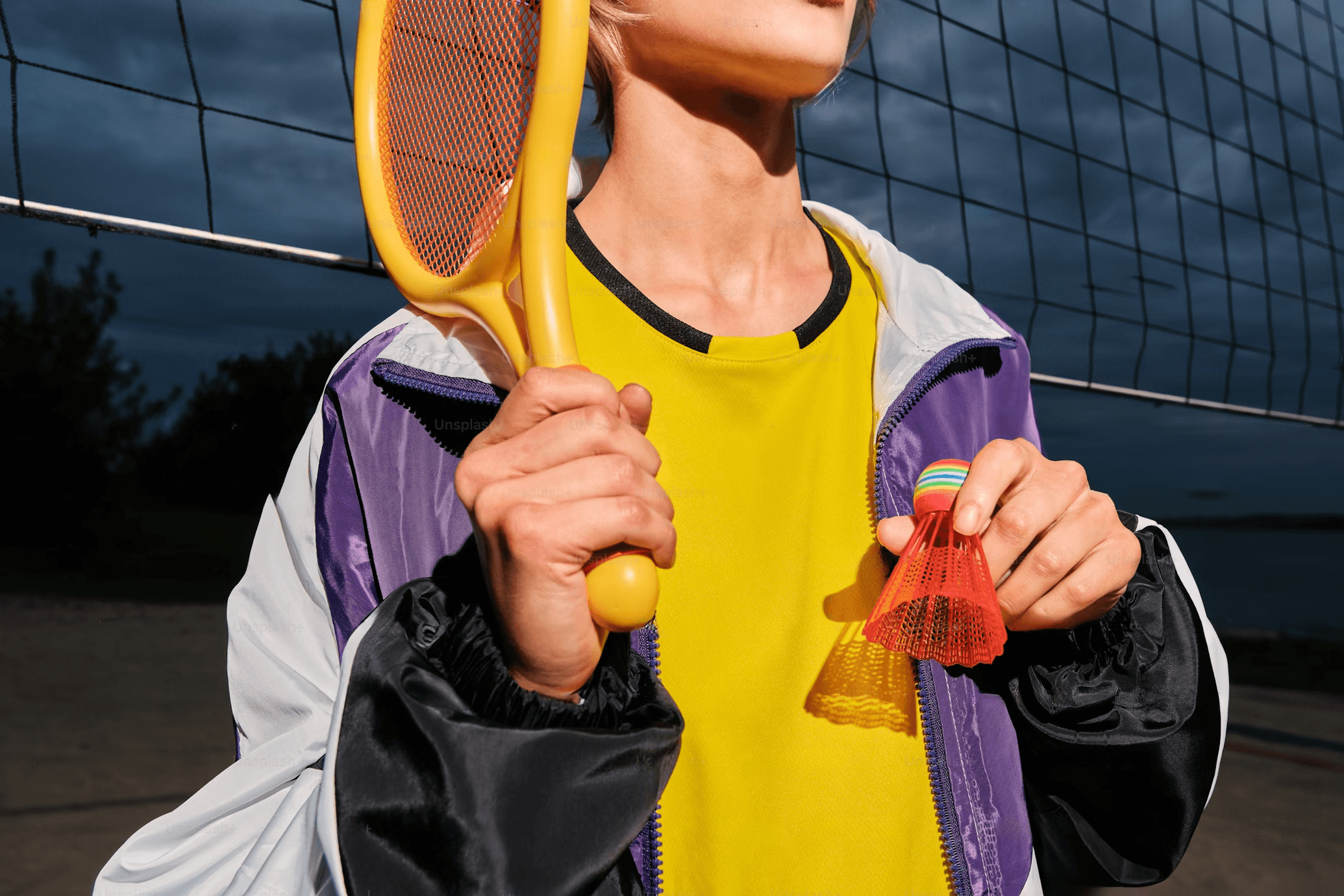 Focused young man in a mint green jacket staring ahead, with a fencing sword vertically aligned with his face, rooftops of a European city in the background.