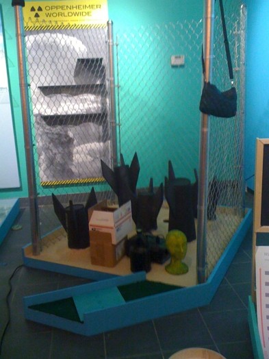 installation view of a sculpture mad with the end of rocket shapes on a wooden floor and a metal wire fence installer all around them